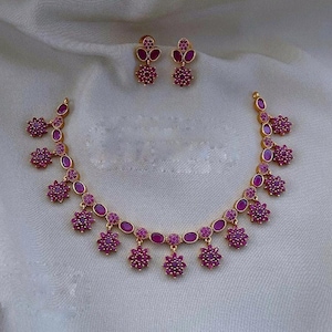 Op de afbeelding: Een gouden ketting met roze edelsteen accenten. De ketting heeft een delicate ketting met hangende bloemvormige bedels. De ketting wordt geleverd met bijpassende oorbellen.
