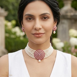 May include: A multi-strand pearl choker necklace featuring a central circular pendant encrusted with small red stones and a single dangling pearl, accompanied by matching circular stud earrings with red stones and a single dangling pearl.