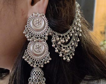 May include: Silver-toned statement earrings with a floral design and dangling beads. The earrings feature a layered design with a chain that attaches to the hair. The earrings are worn on the ear.