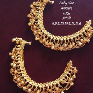 May include: Two gold-toned metal anklets featuring a chain-link design with dangling spherical charms and a screw-style clasp. Text on the image reads: Baby size Anklets 6,7,8 Adult 9,9.5,10,10.5,11,11.5. The jewellery has a polished metallic finish.