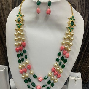 May include: A three-strand necklace featuring green and pink beads, with a gold pendant adorned with green stones. Matching earrings with pink and green stones are also included.