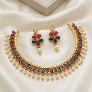 May include: A gold-toned necklace and matching earring set featuring teardrop-shaped fuchsia and emerald green stones, accented with small white pearls and clear crystals arranged in a floral pattern on the earrings.