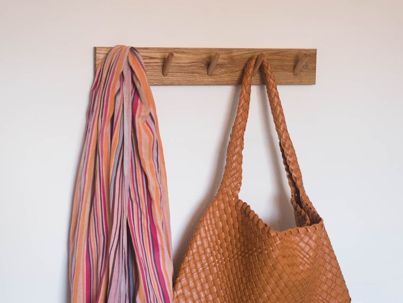 May include: A wooden wall-mounted coat rack with four hooks. A striped scarf and a brown leather bag are hanging on the hooks.