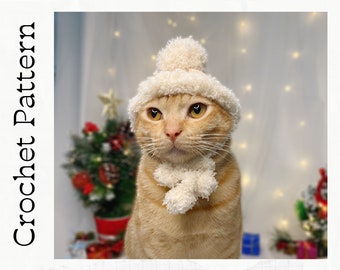 Puede incluir: Primer plano de un gato jengibre con un gorro y una bufanda de ganchillo blancos. El gato mira directamente a la cámara con una expresión seria. El fondo está desenfocado y presenta un árbol de Navidad y luces.