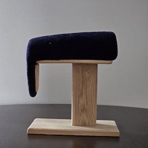 Könnte beinhalten: Eine dunkelblaue gepolsterte Armlehne mit einem Holzsockel und einem Holzständer. Die Armlehne ist mit einer Holzhalterung am Ständer befestigt.