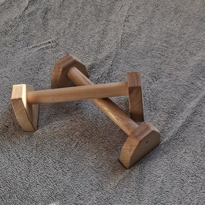 Op de afbeelding: Twee houten parallelle stangen voor oefeningen, gekruist over elkaar, op een grijs, pluche oppervlak.