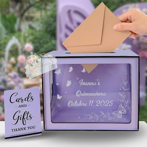 May include: A lavender card box with a slot for inserting cards, decorated with butterfly designs and the text "Iovanna's Quinceañera October 11, 2025." A small sign reads "Cards and Gifts Thank You."