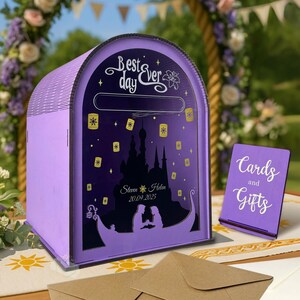 A personalized wooden wedding card box with a fairytale, royal theme and a purple color.

The intricate sun design and the couple's names and date are engraved on the front of the card box.

A close-up of the slot on top of the box, where cards can be placed.