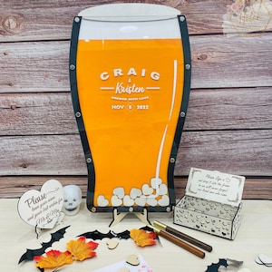 May include: A wooden beer glass shaped wedding guest book with a clear acrylic panel for guests to sign their well wishes. The glass is filled with white wooden hearts. The glass is decorated with the names "Craig & Kristen" and the date "Nov 5 2022".