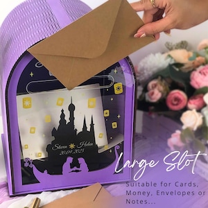 May include: A purple and clear acrylic wedding card box with a castle silhouette design. The box has a large slot for cards and envelopes. The text on the box reads "Steven & Helen 20.09.2025". A brown envelope is being inserted.