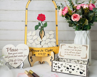 May include: A wooden wedding guest book with a glass dome and a red rose inside. The guest book is decorated with hearts and the names "Bryant & Taylor" and the date "9/9/22".