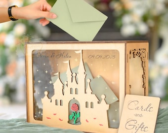 May include: A wooden card box with a castle design, a red rose, and the words "Cards and Gifts." An envelope is being placed into the box. The box is personalized with names and a date.