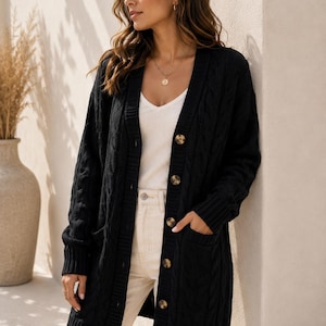 May include: A black long-sleeve cable knit cardigan featuring a V-neckline, a front button closure with brown buttons, and two front patch pockets. The garment has ribbed cuffs and a ribbed hem, providing a structured fit with a textured pattern.