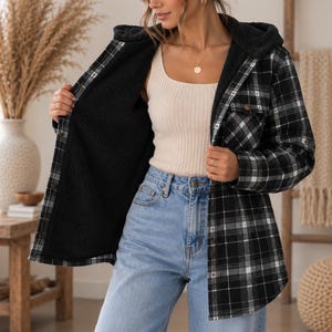 May include: A black and white plaid hooded jacket with a black sherpa lining, worn over a beige ribbed tank top and light blue denim jeans. The jacket features a button-front closure, long sleeves with buttoned cuffs, and two chest pockets.
