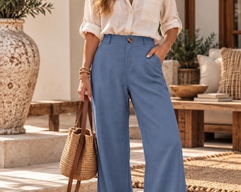 May include: A beige long-sleeved button-down shirt with a collar and a chest pocket paired with high-waisted, wide-leg blue trousers featuring a single button closure and side pockets. The outfit is completed with tan slide sandals.