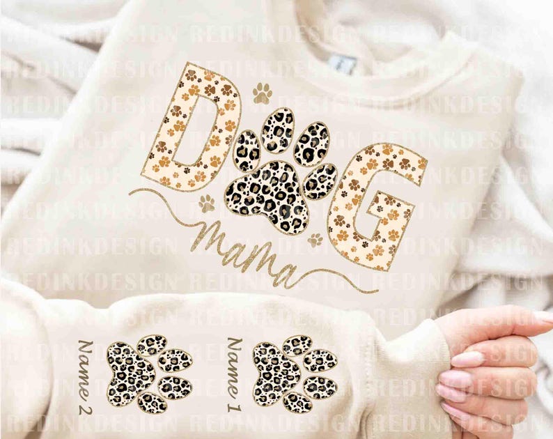 May include: A white sweatshirt with the words "Dog Mama" in gold letters with a leopard print design. The letters are surrounded by paw prints. The sweatshirt has two blank spaces for names with leopard print paw prints.