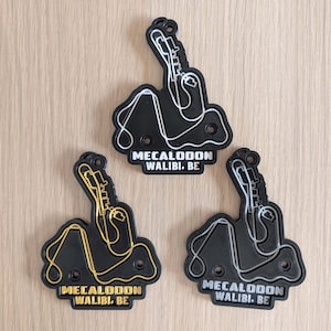 May include: Three black keychains with a roller coaster design and the text "MECALODON WALIBI. BE" in white, gold, and silver. The keychains are made of a solid material and have a hole for attaching to a keyring.