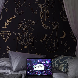 Puede incluir: Un tapiz negro y dorado con un tema celestial. El tapiz presenta un gato, una luna, estrellas, cristales y una botella con constelaciones. El tapiz está colgado en una pared detrás de una cama con una computadora portátil encima. La pantalla de la computadora portátil muestra un fondo brillante con la palabra "Dream" escrita en ella.