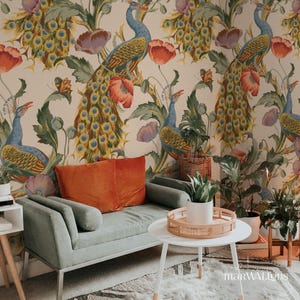 May include: A living room scene featuring a sage green loveseat with an orange velvet pillow. A white coffee table holds a woven tray with a potted plant. The backdrop is a floral wallpaper with peacocks, poppies, and butterflies.