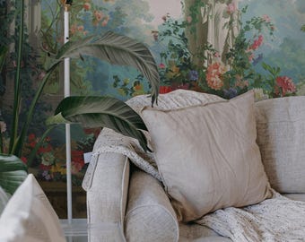 May include: A light gray couch with a throw blanket and a pillow. The couch is in front of a wall with a floral wallpaper featuring a statue of a woman in a garden setting. The wallpaper has a blue, green, and pink color scheme.