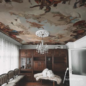 Könnte beinhalten: Innenraum mit bemalter Decke mit Figuren und Wolken. Ein Kristall-Kronleuchter hängt von der Decke. Dunkle Holzschränke und eine Bank mit einer Decke befinden sich darunter. Der Raum hat eine Vintage-Ästhetik.