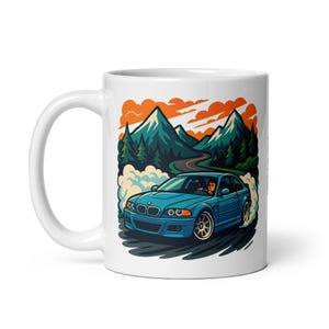 May include: White ceramic mug featuring a blue BMW M3 driving on a winding road through a mountainous landscape. The car is creating smoke as it drifts around a bend.