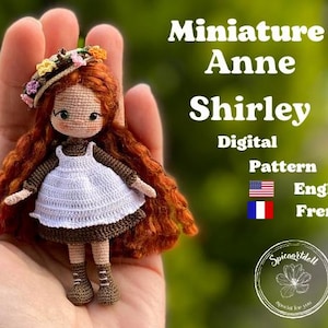 Könnte beinhalten: Häkelanleitung für eine Miniatur-Puppe Anne Shirley. Die Puppe trägt ein weißes Kleid mit braunem Oberteil und einem Blumen-Haarreif. Die Anleitung ist in Englisch und Französisch verfügbar.