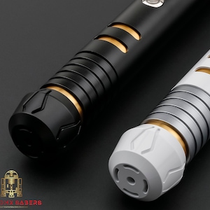 K&ouml;nnte beinhalten: Zwei futuristische Lichtschwerter, eines in Schwarz und eines in Wei&szlig;, mit goldenen und silbernen Akzenten. Die Griffe haben ein detailliertes Design mit Rillen und geometrischen Mustern. Das Bild ist vor einem dunklen Hintergrund gehalten, der das schlanke Design der Waffen hervorhebt.