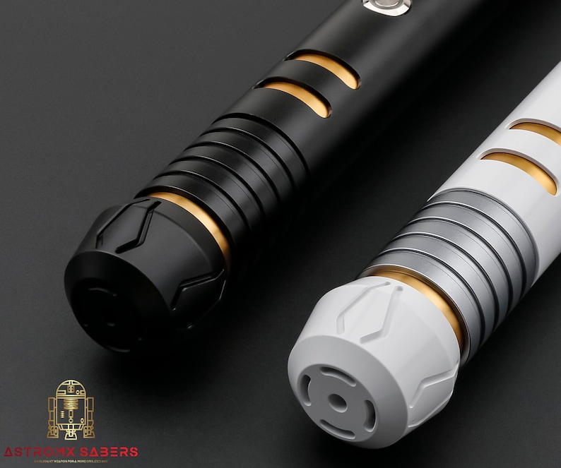 K&ouml;nnte beinhalten: Zwei futuristische Lichtschwerter, eines in Schwarz und eines in Wei&szlig;, mit goldenen und silbernen Akzenten. Die Griffe haben ein detailliertes Design mit Rillen und geometrischen Mustern. Das Bild ist vor einem dunklen Hintergrund gehalten, der das schlanke Design der Waffen hervorhebt.