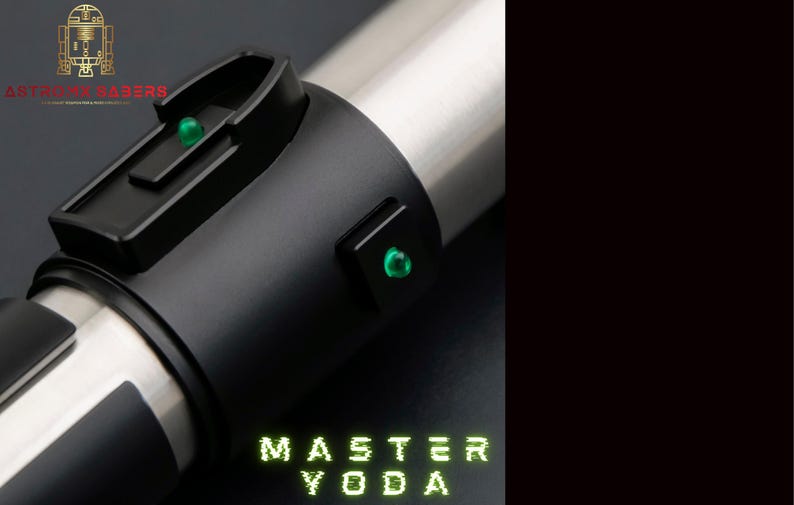 May include: A lightsaber with a black handle and silver details. It features two green lights and the text "MASTER YODA" in green. The "ASTRO SABERS" logo is visible in the top left corner.