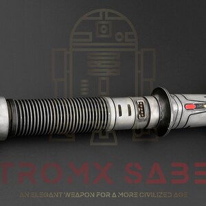 Puede incluir: Un sable de luz plateado y negro con un emisor dorado y un bot&oacute;n rojo. El sable de luz es una r&eacute;plica de un arma ficticia de la franquicia Star Wars. El texto "ASTROMYX SABERS" es visible en rojo en la parte inferior de la imagen. El texto "AN ELEGANT WEAPON FOR A MORE CIVILIZED AGE" es visible en rojo en la parte inferior de la imagen.