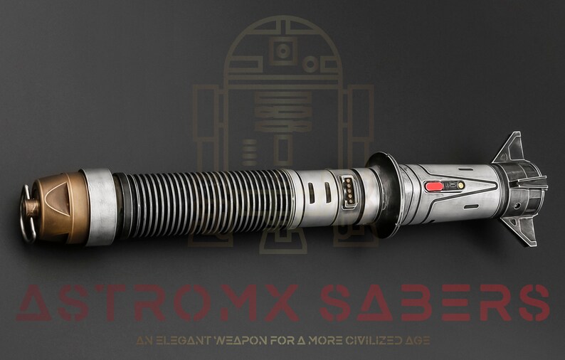 Puede incluir: Un sable de luz plateado y negro con un emisor dorado y un bot&oacute;n rojo. El sable de luz es una r&eacute;plica de un arma ficticia de la franquicia Star Wars. El texto "ASTROMYX SABERS" es visible en rojo en la parte inferior de la imagen. El texto "AN ELEGANT WEAPON FOR A MORE CIVILIZED AGE" es visible en rojo en la parte inferior de la imagen.