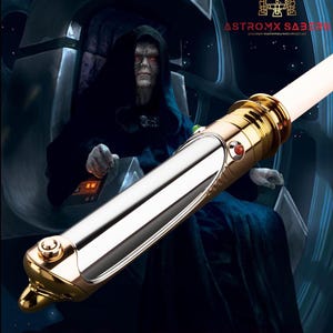 May include: A gold and silver lightsaber with a white blade, set against a dark background featuring a character in a black robe. The text "LORD SIDIOUS" is displayed at the bottom, with the "ASTROMX SABERS" logo at the top.