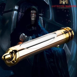 May include: A gold and silver lightsaber with a detailed hilt is featured in this image. The lightsaber is set against a dark background with a character in a dark robe. The text "LORD SIDIOUS" is at the bottom of the image.