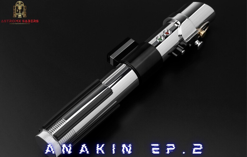 May include: A metallic silver and black lightsaber with the text "ANAKIN EP. 2" in blue. The lightsaber has a detailed design with buttons and a control panel. The logo "ANTROX SABERS" is in the upper left corner.