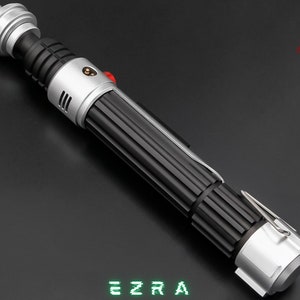 May include: A detailed lightsaber prop with a black ribbed handle, silver accents, and a red button. The text "EZRA" is displayed in green, pixelated font. The logo for "ASTROMX SABERS" is in the upper right corner.