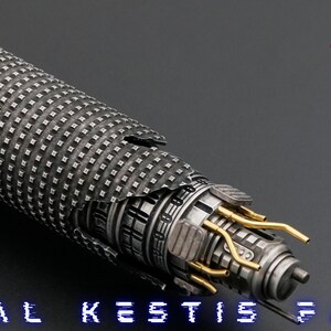 K&ouml;nnte beinhalten: Ein silbernes Lichtschwert mit einem schwarz-silbernen Griff und einer goldfarbenen Klinge. Das Lichtschwert ist in zwei Teile zerbrochen, wodurch die inneren Mechanismen der Waffe sichtbar werden. Der Text "CAL KESTIS F/O" ist am unteren Rand des Bildes zu sehen.