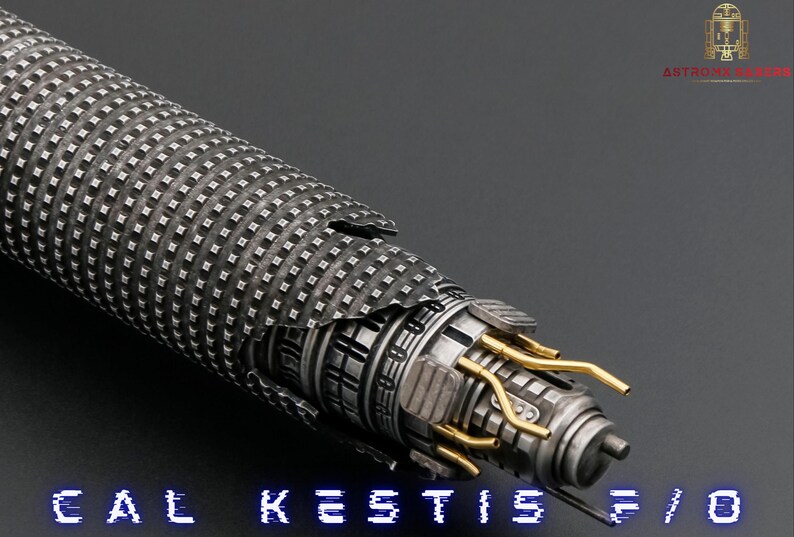 K&ouml;nnte beinhalten: Ein silbernes Lichtschwert mit einem schwarz-silbernen Griff und einer goldfarbenen Klinge. Das Lichtschwert ist in zwei Teile zerbrochen, wodurch die inneren Mechanismen der Waffe sichtbar werden. Der Text "CAL KESTIS F/O" ist am unteren Rand des Bildes zu sehen.