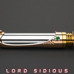 May include: A lightsaber with a gold and silver finish, featuring a green gem and the text "LORD SIDIOUS". The hilt has intricate detailing and a sleek design, with a gold-colored pommel and emitter.