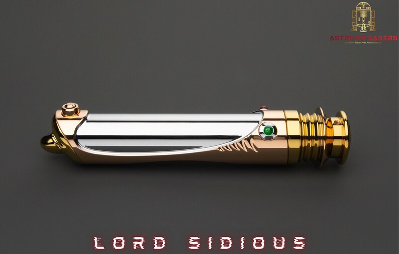 May include: A lightsaber with a gold and silver finish, featuring a green gem and the text "LORD SIDIOUS". The hilt has intricate detailing and a sleek design, with a gold-colored pommel and emitter.