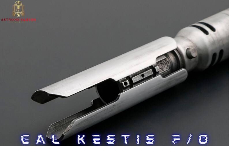 K&ouml;nnte beinhalten: Ein silberner Lichtschwertgriff mit einem schwarzen Griff und einer silbernen Klinge. Der Griff hat eine Reihe kleiner, runder L&ouml;cher und einen schwarzen Knopf an der Seite. Der Text "CAL KESTIS F/O" ist am unteren Rand des Bildes sichtbar.