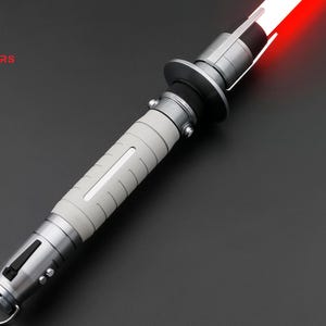 May include: A silver lightsaber hilt with a white grip and a red blade. The hilt has a black ring around the middle and a silver button on the side.