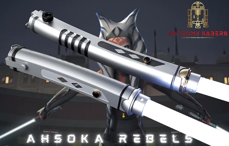May include: Two silver lightsabers with white blades are displayed against a blurred background featuring a character from the Star Wars franchise. The lightsabers have black and silver accents and the text "AHSOKA REBELS" is visible.