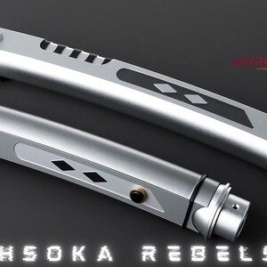 May include: Two silver lightsabers with black and gold accents, featuring a diamond pattern and the text "AHSOKA REBELS." The lightsabers have a sleek, metallic design, with a gold-colored end cap. The image also includes a gold logo.