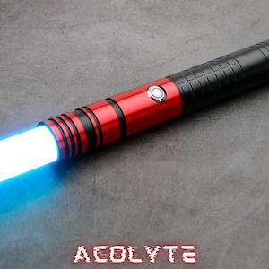 May include: A red and black lightsaber with a blue blade. The lightsaber has a silver button and the word "ACOLYTE" is printed on the surface below it.
