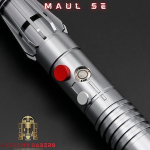 Op de afbeelding: Een zilveren lichtzwaard met een rode knop en een zilveren bedieningspaneel. De tekst "MAUL SE" staat bovenaan. De onderkant van het lichtzwaard heeft de tekst "ASTRO MX SABERS" en een gouden robotafbeelding.