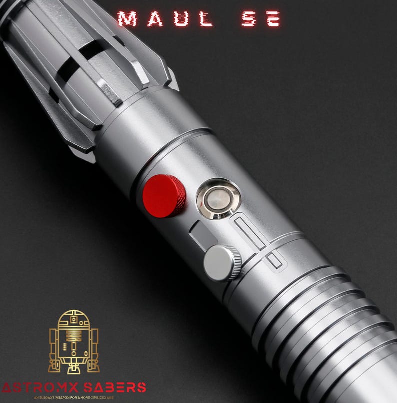 Op de afbeelding: Een zilveren lichtzwaard met een rode knop en een zilveren bedieningspaneel. De tekst "MAUL SE" staat bovenaan. De onderkant van het lichtzwaard heeft de tekst "ASTRO MX SABERS" en een gouden robotafbeelding.