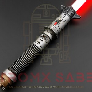 Puede incluir: Un sable de luz rojo con una empu&ntilde;adura plateada y negra. La empu&ntilde;adura tiene un agarre texturizado y un bot&oacute;n rojo. El sable de luz est&aacute; encendido y la hoja es roja. El sable de luz est&aacute; sobre un fondo gris oscuro.