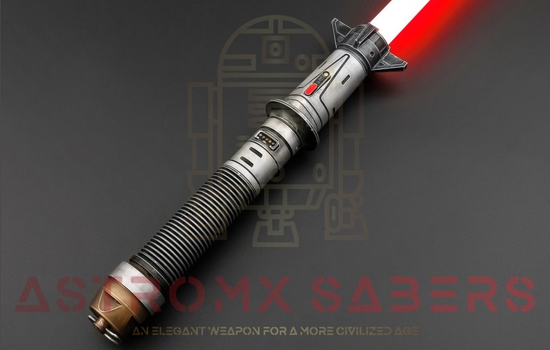 Puede incluir: Un sable de luz rojo con una empu&ntilde;adura plateada y negra. La empu&ntilde;adura tiene un agarre texturizado y un bot&oacute;n rojo. El sable de luz est&aacute; encendido y la hoja es roja. El sable de luz est&aacute; sobre un fondo gris oscuro.