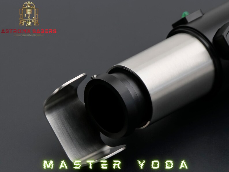 May include: A lightsaber hilt with a silver and black design is shown in close-up. The lightsaber has a cylindrical body with a silver finish and a black grip. The text "MASTER YODA" is displayed in green at the bottom.